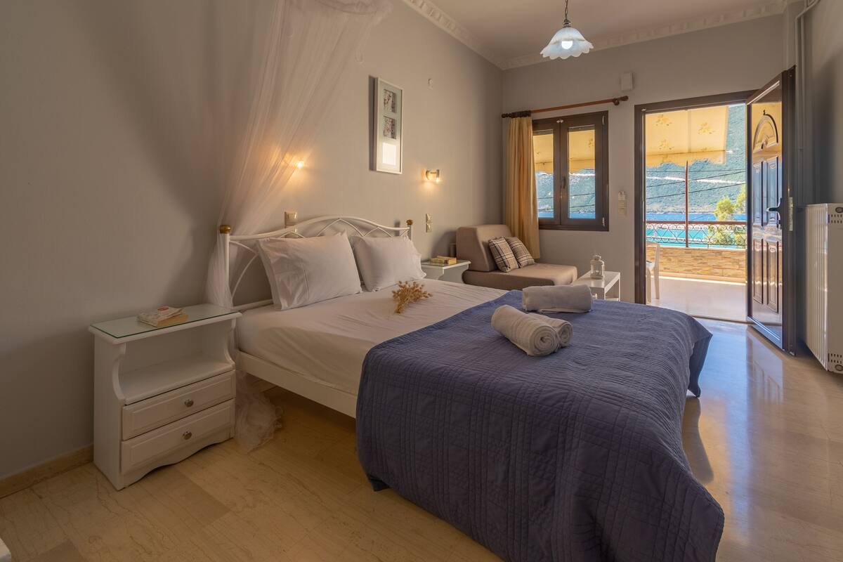 A bedroom with a bed, nightstands, a chair, and a view of the outdoors.