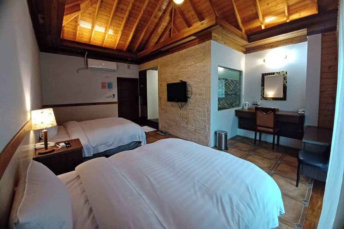 A hotel room with two beds, a desk, a chair, a mirror, and a window.