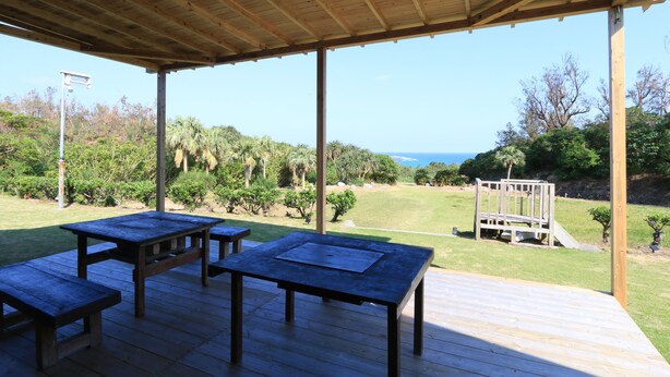 An outdoor wooden deck with picnic tables, a wooden play structure, and a view of the ocean. - Rest and Lodge Syou (Amami)