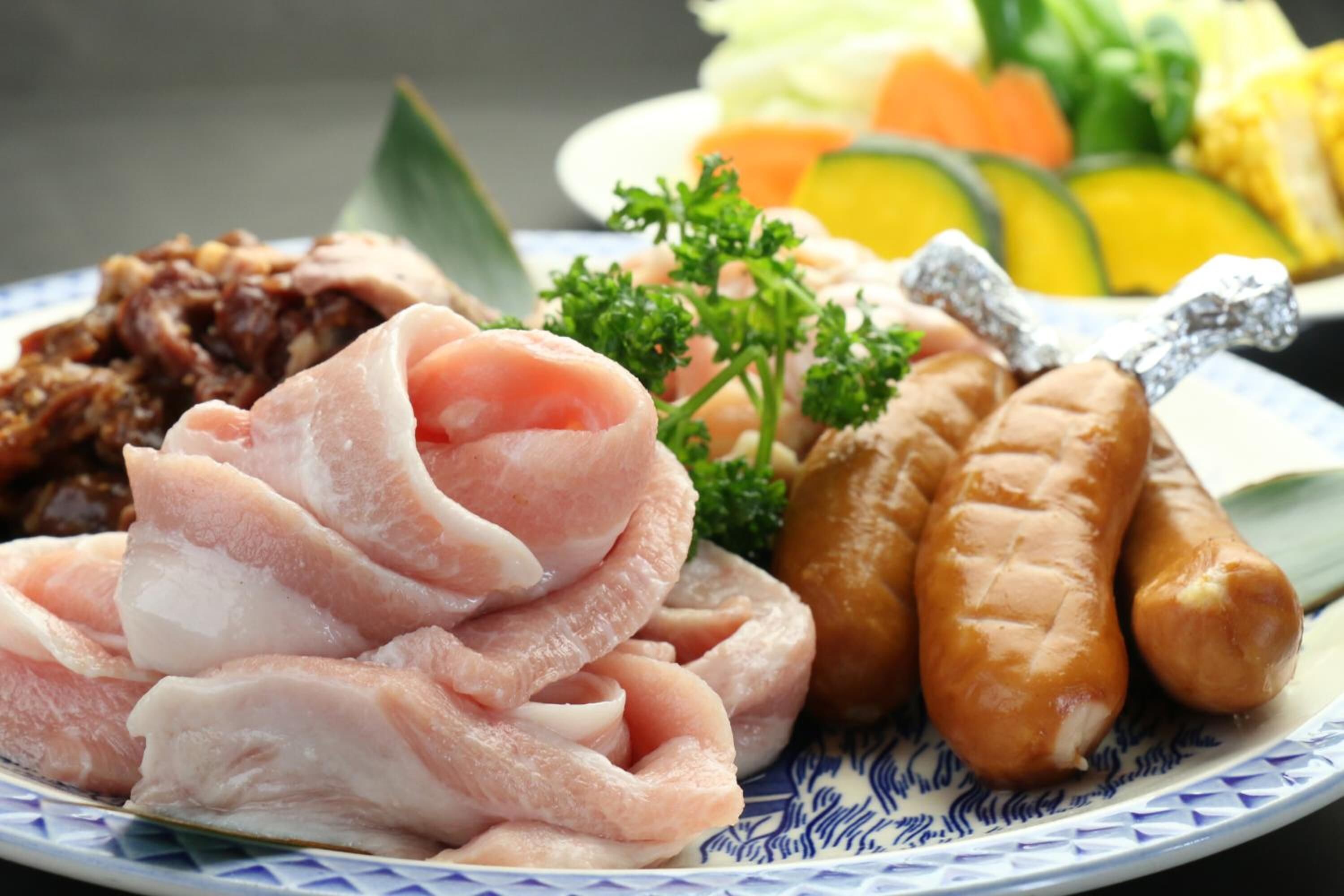 Un plato con diversos alimentos, incluyendo carne en rodajas, salchichas y verduras.