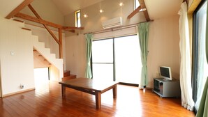 A spacious room with wooden flooring, a staircase, a flat-screen TV, and a large window with curtains. - Rest and Lodge Syou (Amami)