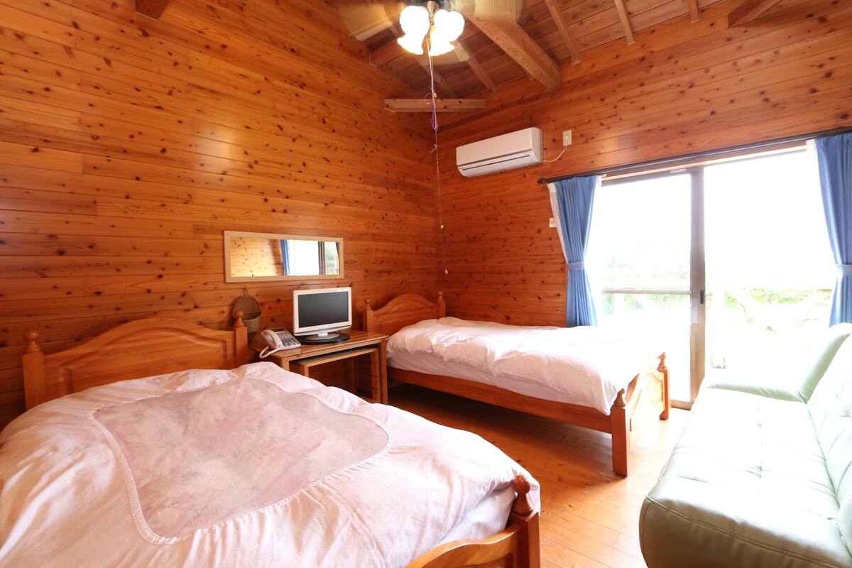 A wooden cabin room with two beds, a desk with a computer, and a sofa.