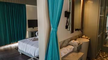 A hotel room with a bed, a bathroom with a sink and mirror, and teal curtains.