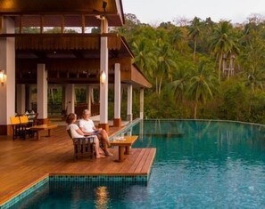 Une terrasse en bois avec une piscine, entourée de palmiers.