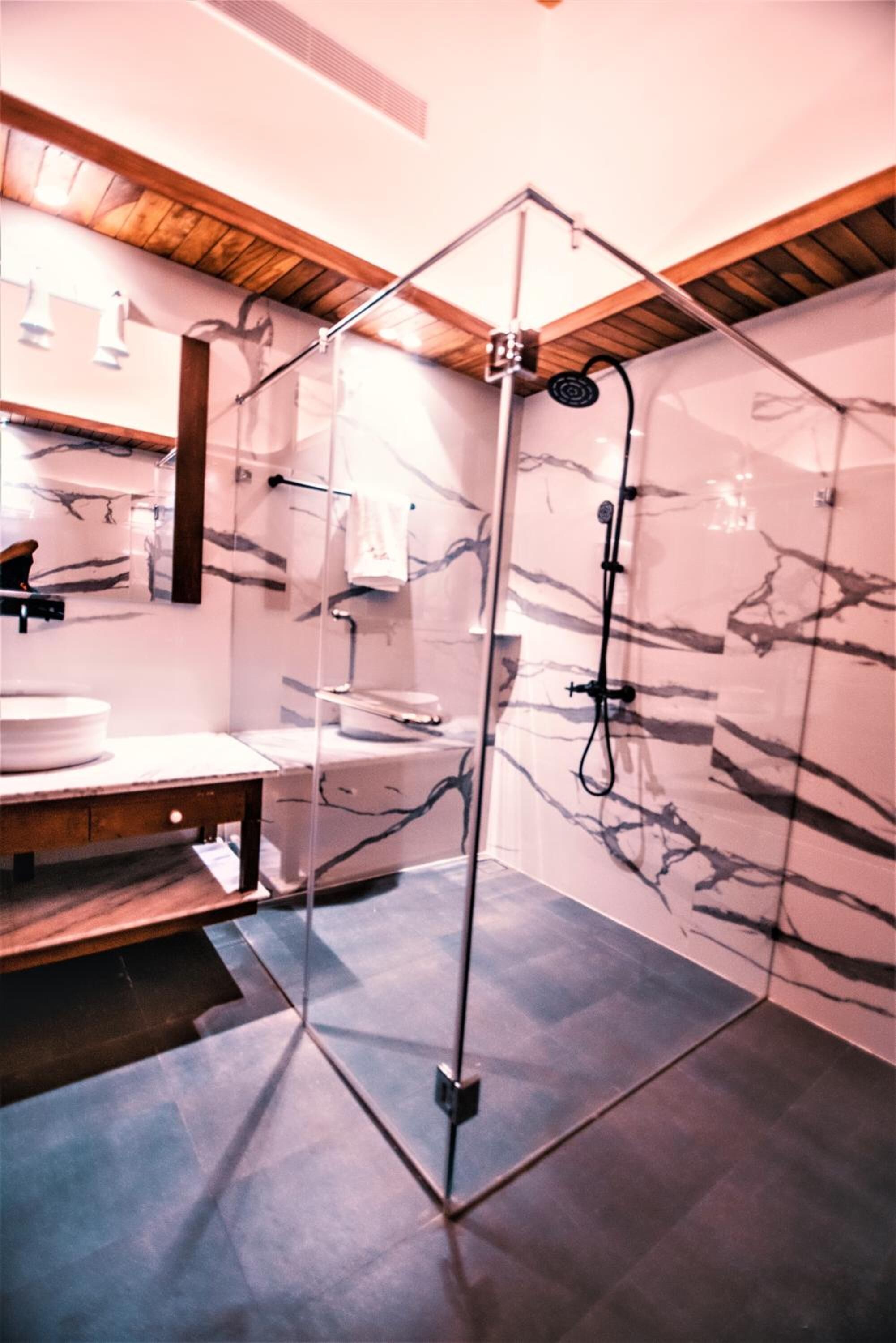 Un baño moderno con ducha de vidrio, paredes de mármol y vigas de madera en el techo.