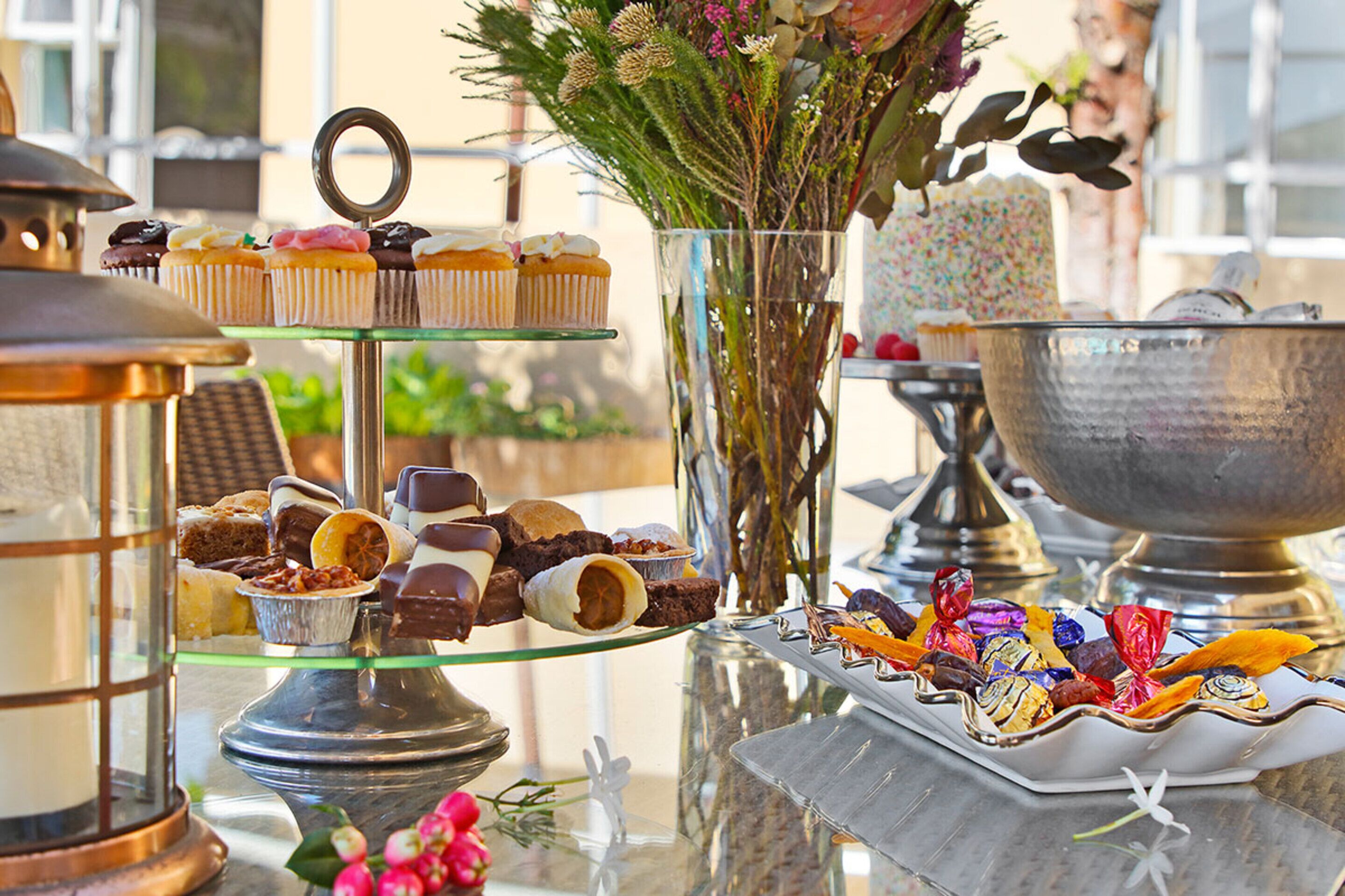 A buffet table with various desserts and a decorative vase with flowers.