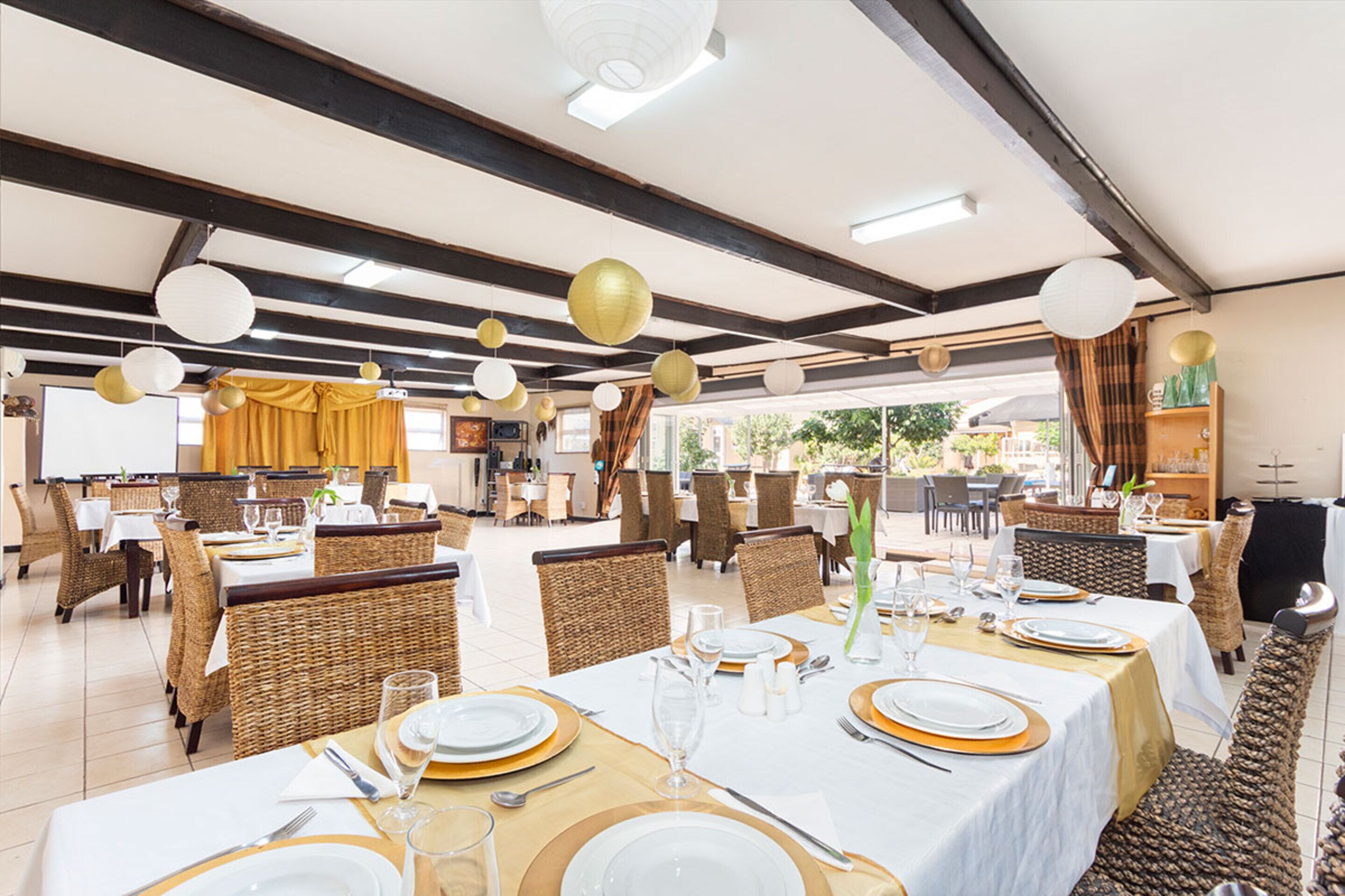 Un vaste espace dédié à la salle à manger, avec plusieurs tables dressées, des chaises en osier et un design moderne au niveau du plafond.