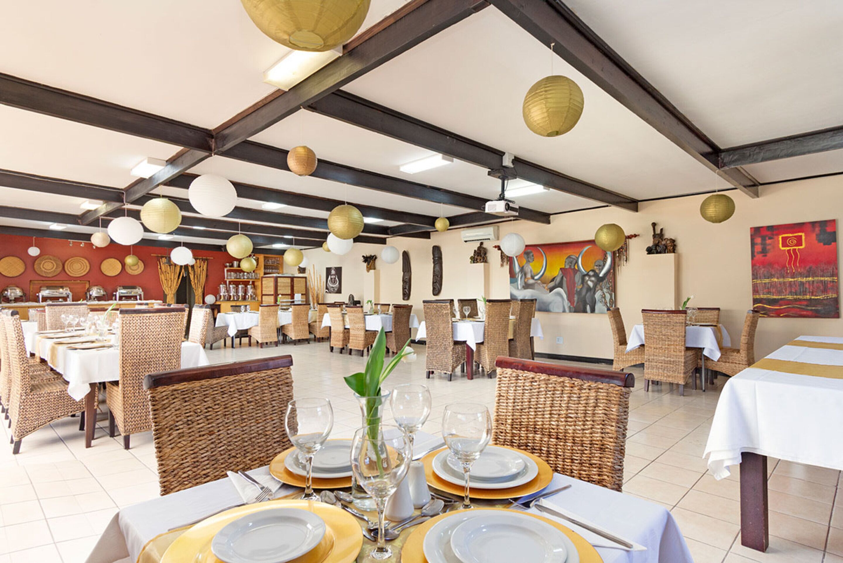 A restaurant with multiple dining tables set with white tablecloths, gold-rimmed plates, and clear glassware.