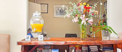 A reception desk with a 'Welcome' sign, a glass container with orange liquid, a vase with flowers, and a bookshelf filled with books and magazines.