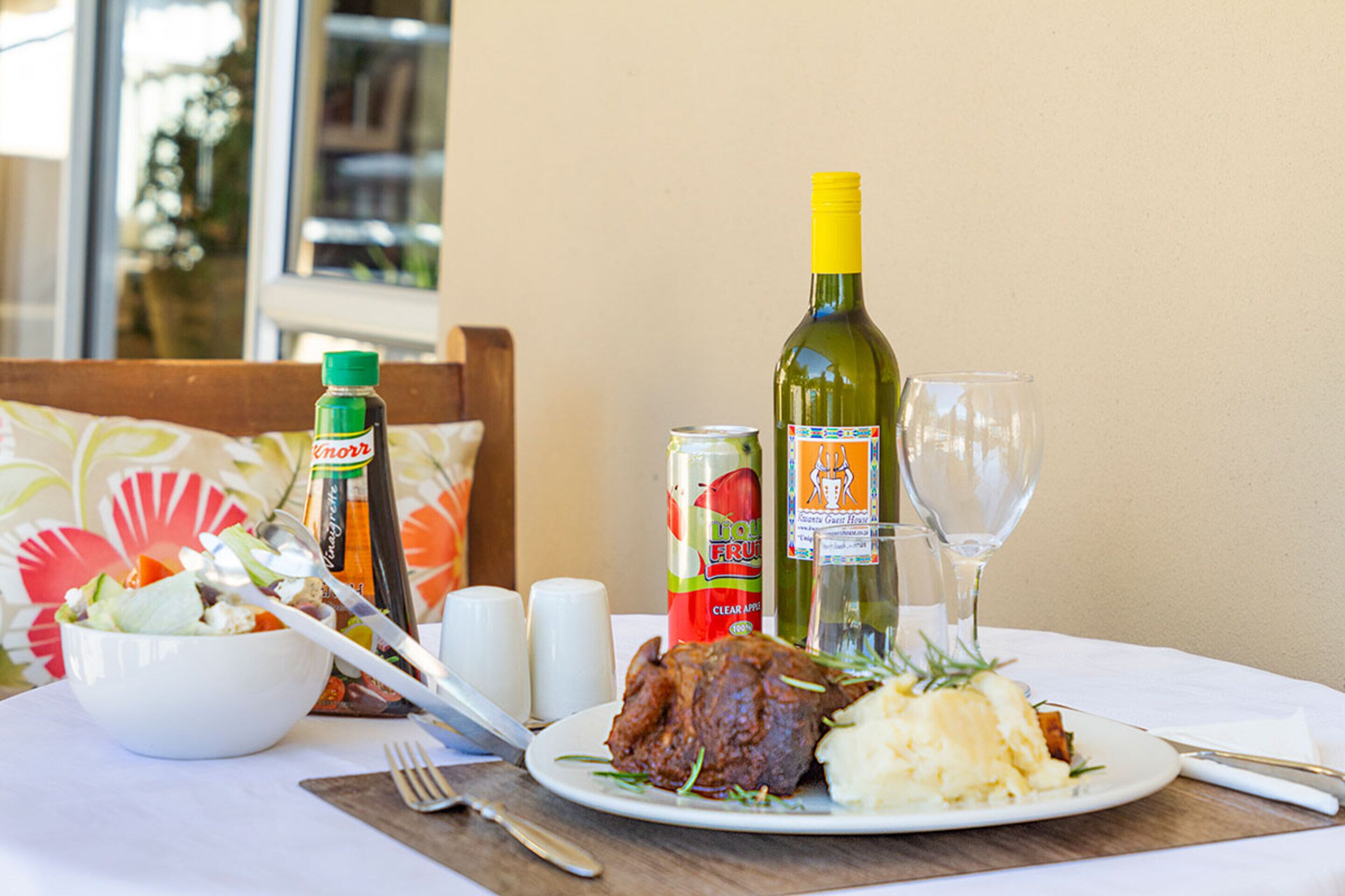 Una mesa de comedor con una ensalada, una lata de refresco de frutas, una botella de vino y una copa de vino.