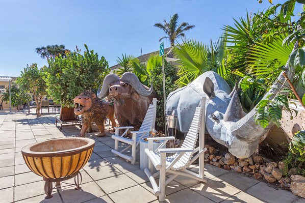 A dinosaur-themed outdoor area with a bull statue, a large white chair, and a stone basin.