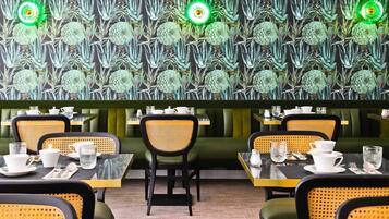 A restaurant with green upholstered booths and yellow wicker chairs, tables set with white dishes and glasses.