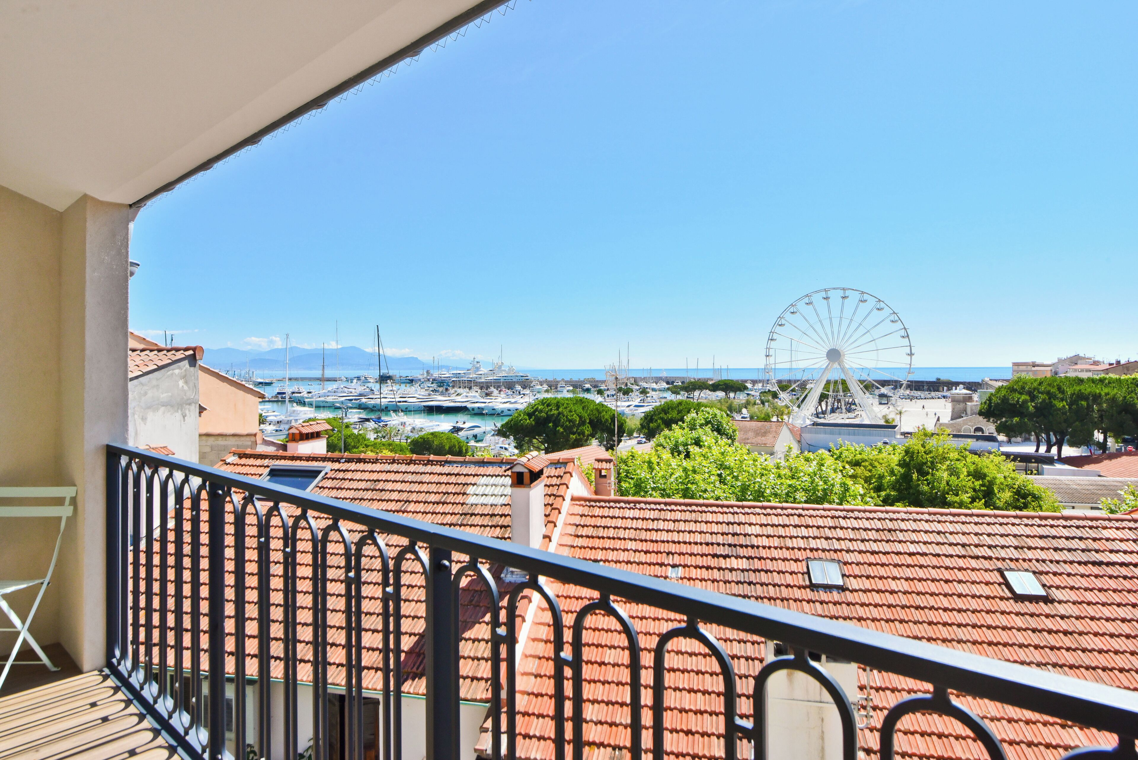 Un balcone con vista su un porto turistico, una ruota panoramica e un cielo azzurro limpido.