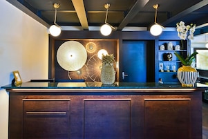 Un mostrador de recepción con diseño moderno, con detalles de madera y una superficie de vidrio. Tres lámparas colgantes iluminan el mostrador, y un centro de mesa decorativo con una piña.