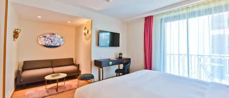 Une chambre d’hôtel comprenant un lit, un canapé, un bureau, une télévision et un balcon avec une balustrade.