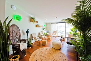 Una sala de estar moderna con un ventanal grande, pisos de madera y diferentes opciones de asientos, incluyendo un sofá y sillones.