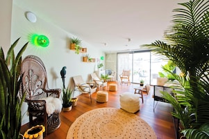 A modern living room with a large window, wooden flooring, and various seating options including a sofa and chairs.