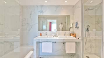 Un baño moderno con paredes de mármol, un espejo grande, dos lavamanos y una zona de ducha con mampara de vidrio.