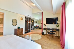 A modern hotel room with a large bed, a desk with a chair, a TV, and a wardrobe.