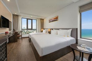 A hotel room with a large bed, a desk, a TV, and a view of the city and ocean. - Santa Luxury Hotel (Da Nang)
