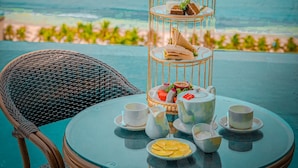 A table set with tea and snacks, a wicker chair, and a decorative birdcage with treats, overlooking a beach. - Santa Luxury Hotel (Da Nang)