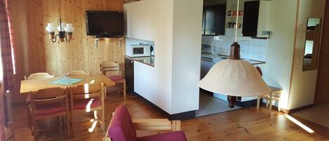 A cozy, compact living space with a dining area, kitchenette, and a TV mounted on the wall.