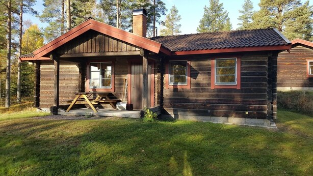 Hirsimökki, jossa on katettu kuisti, savupiippu ja piknikpöytä.