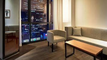 Una sala de estar moderna con un sofá, un sillón y una mesa de centro, que ofrece vistas a la ciudad a través de amplios ventanales.