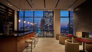 Un bar moderno con vistas a la ciudad, que incluye una barra, taburetes y mesas redondas.