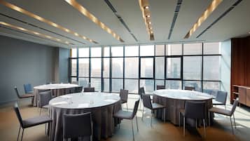 A conference room with round tables and chairs, large windows with a city view, and modern lighting fixtures.