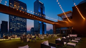 Un salón en la azotea con asientos exteriores y vistas del horizonte de la ciudad al atardecer.