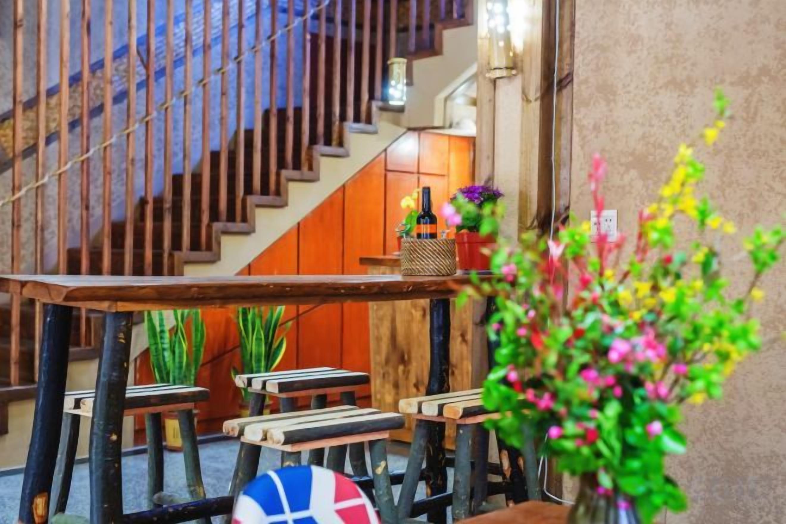 A wooden staircase with a bench and a table with a bottle and flowers.