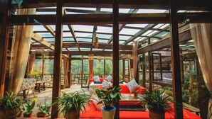 A sunlit room with wooden beams, red seating, and potted plants. - Guyue Caotang (Huzhou)