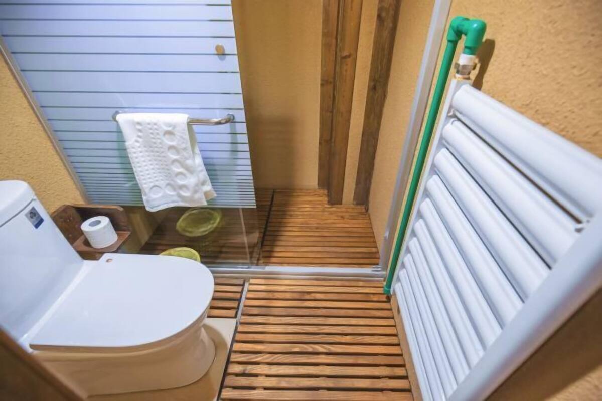 A bathroom with a toilet, a shower, a towel rack, and a radiator.