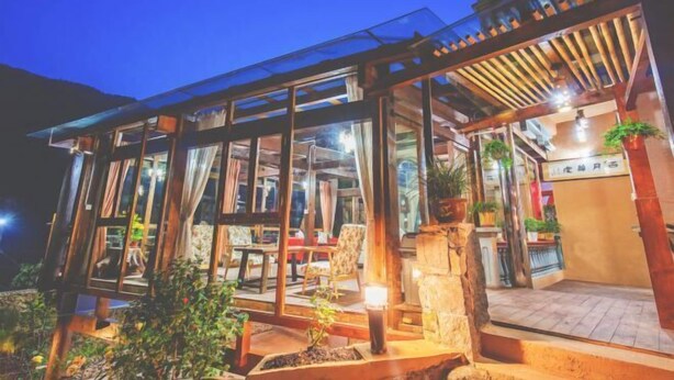 A modern building with large glass windows, outdoor seating, and potted plants. - Guyue Caotang (Huzhou)