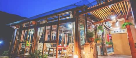 A glass-enclosed building with a wooden deck and outdoor seating area.