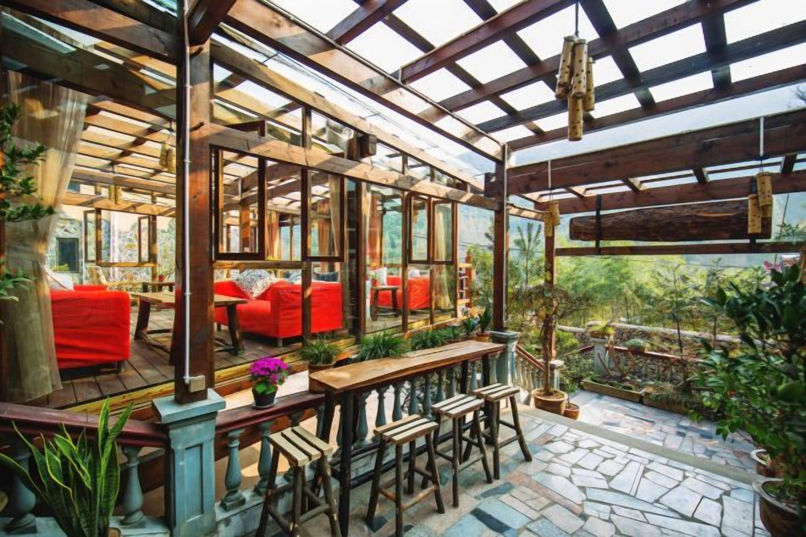 An enclosed patio area with wooden furniture, red cushions, and potted plants.