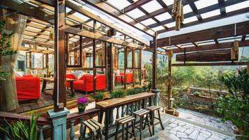 An enclosed patio area with wooden furniture, red cushions, and potted plants.