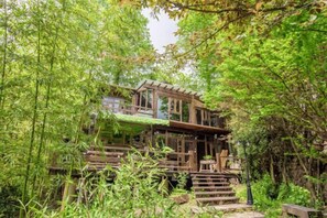 A wooden house with a balcony, surrounded by dense greenery. - Guyue Caotang (Huzhou)