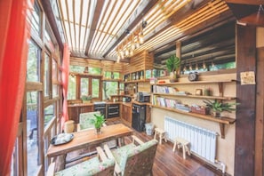 A cozy cabin interior with a dining area, kitchen, and shelves with books and plants. - Guyue Caotang (Huzhou)