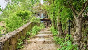 A stone staircase surrounded by lush greenery, leading to a building with a wooden structure. - Guyue Caotang (Huzhou)