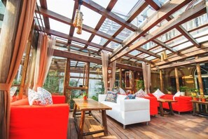 An indoor patio with wooden flooring, red and white furniture, and a glass ceiling allowing natural light. - Guyue Caotang (Huzhou)