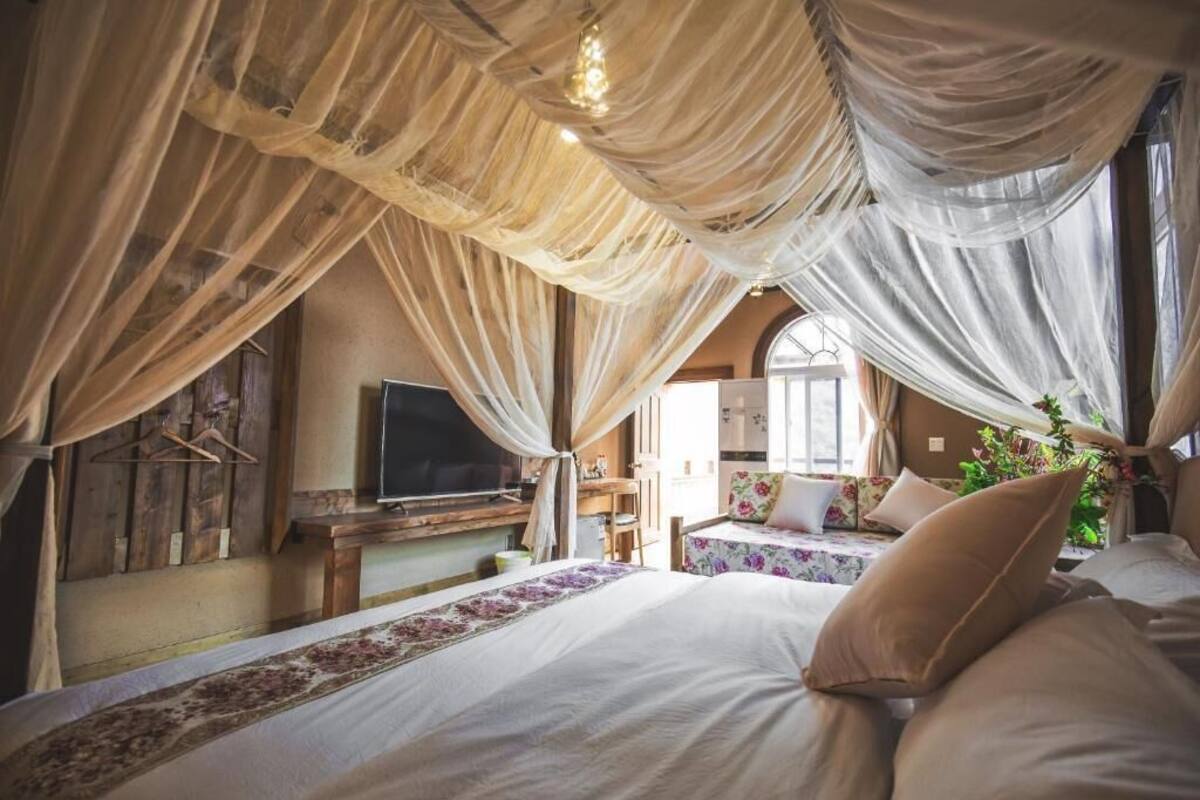 A bedroom with a large bed, a desk with a television, and a window with curtains.