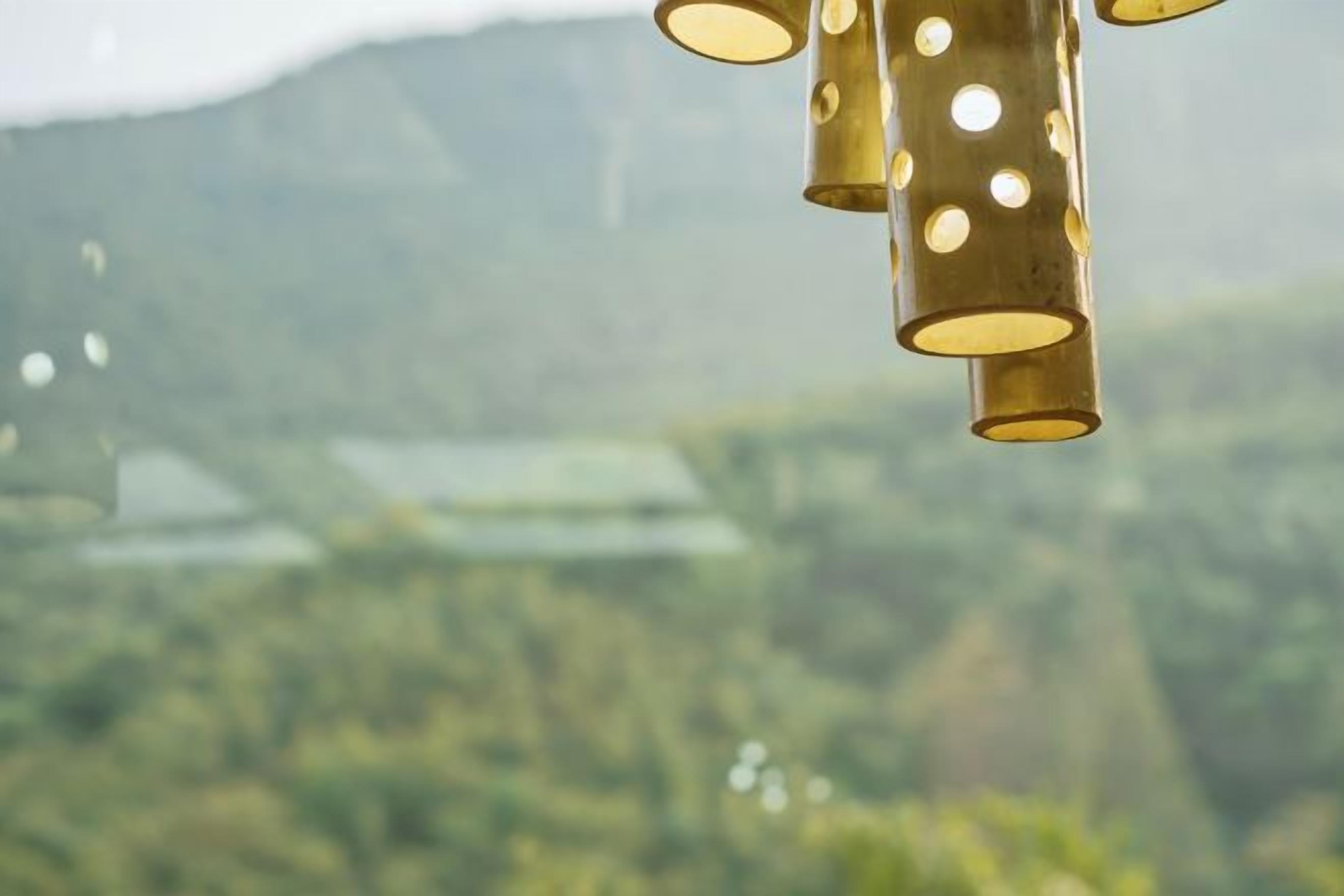 A brass lamp with multiple lights against a blurred background of greenery and hills.