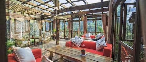 A spacious outdoor area with wooden flooring, red sofas, and a wooden table.