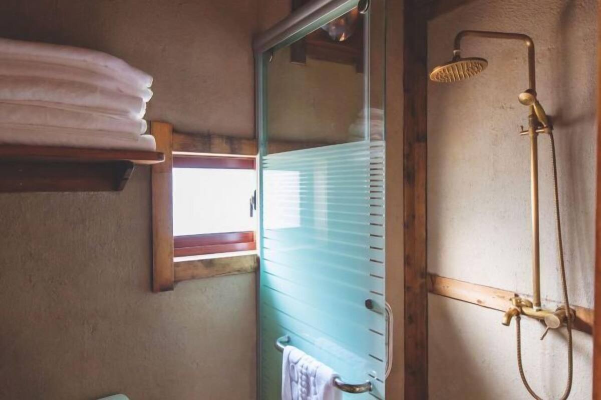 A bathroom with a glass shower enclosure, a towel rack, and a window with blinds.