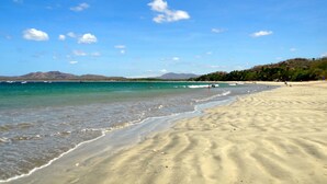 En strand med kristallklart vatten, en sandstrand och berg i fjärran.