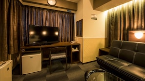 A compact living space with a television, a small refrigerator, a sofa, and a desk. - Sejour Inn Nagarekawa (Hiroshima)