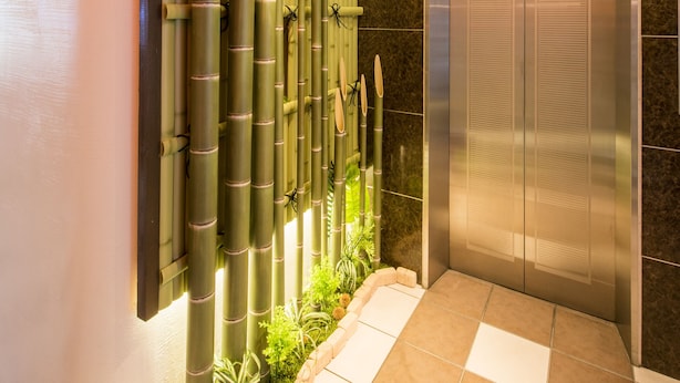 A modern elevator with a metallic finish, surrounded by a bamboo plant wall and a tiled floor. - Sejour Inn Nagarekawa (Hiroshima)