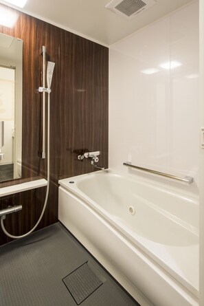 A modern bathroom with a large bathtub, a shower with a handheld showerhead, and a mirror with a towel rack. - Sejour Inn Nagarekawa (Hiroshima)